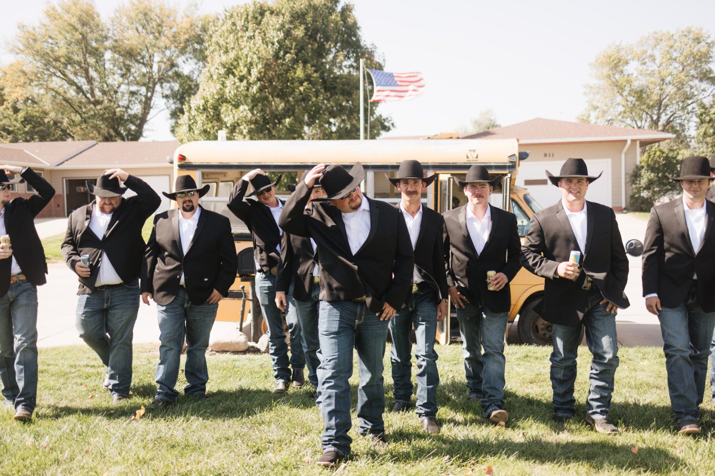 A large group of groomsmen in black suit jackets, jeans, and cowboy hats