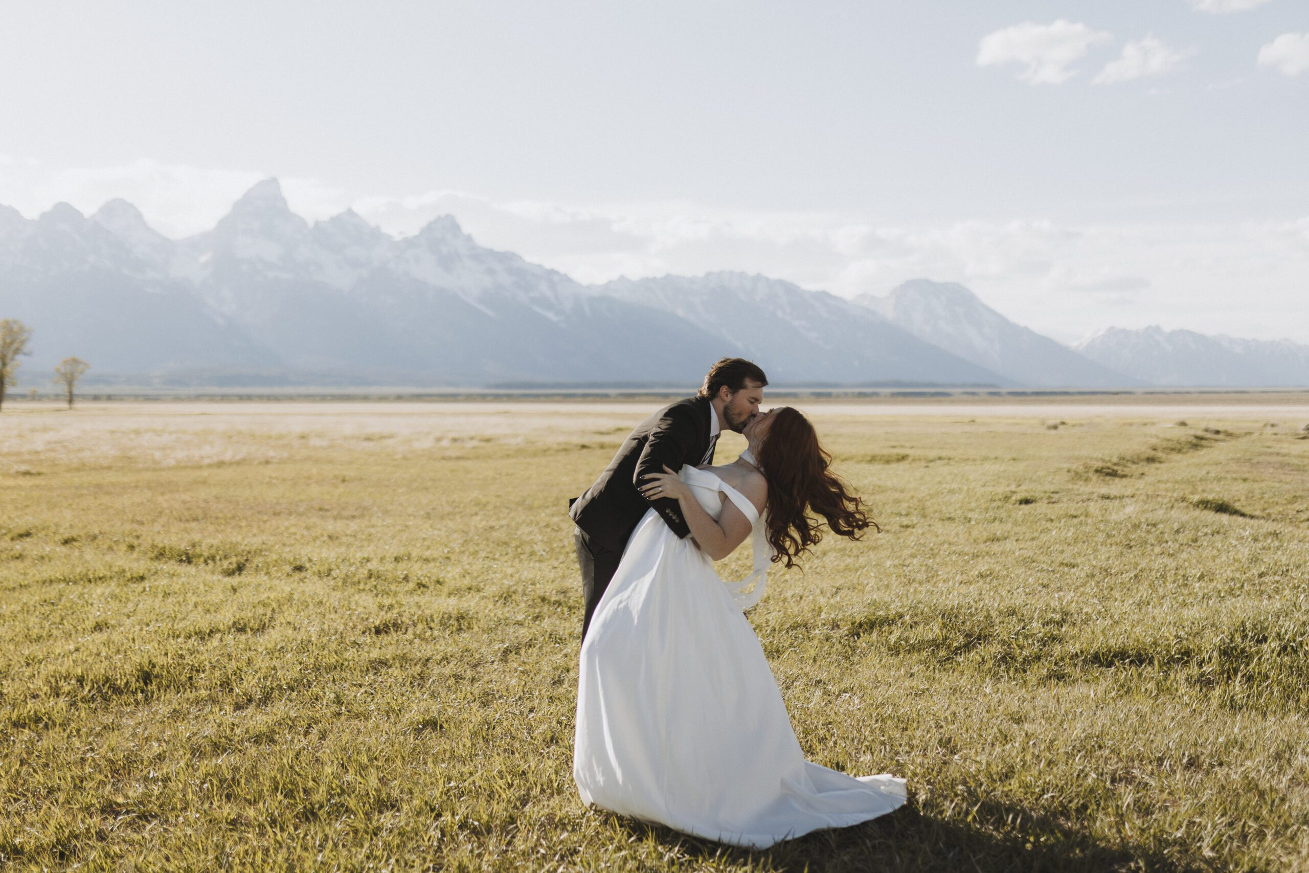 A bride and groom kiss in front of the Teton mountains